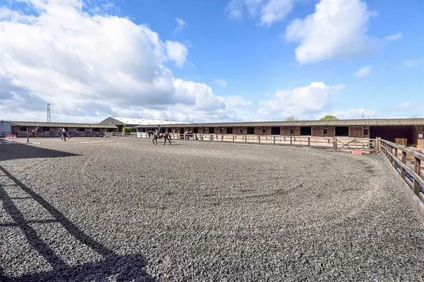 The outdoor arena under a blue sky with stables along one side